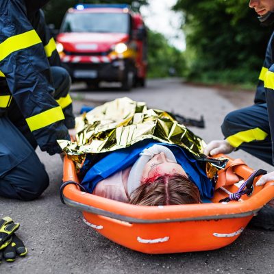 A young injured woman in a plastic stretcher after a car accident, covered by thermal blanket. Close up.