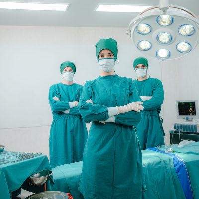 Group of young and experienced male and female surgeon with nurse and doctor wearing scrub, mask and headscarf operating young woman in operation theatre in modern hospital